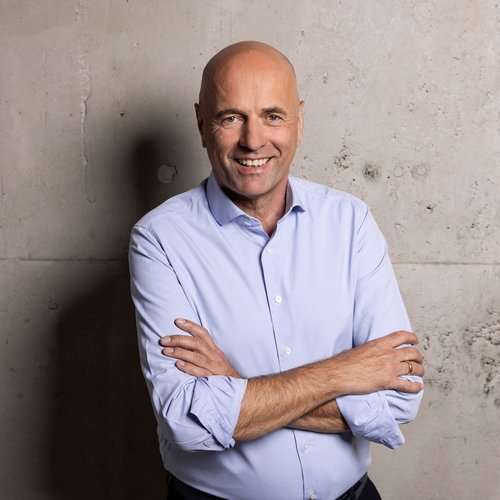 Hans-Jürgen Schweitzer von dimasys steht vor einer Wand und lächelt in die Kamera.